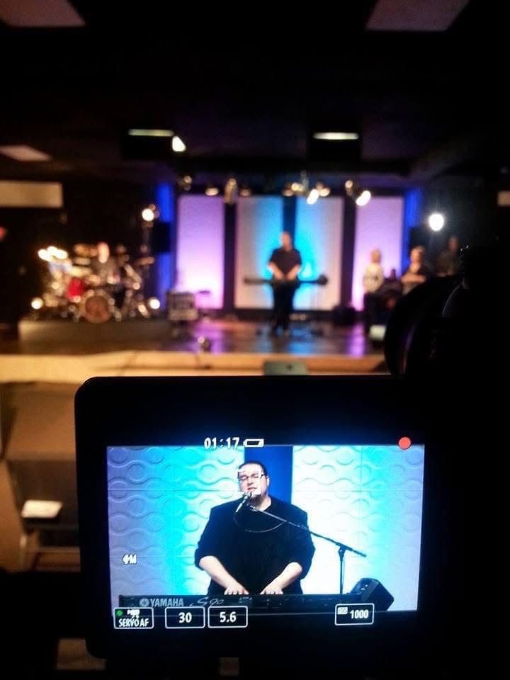 A camera monitor showing Thomas at the keyboard during a church gathering